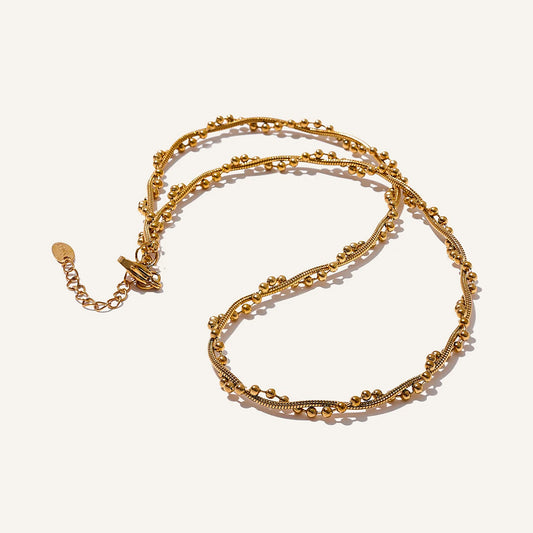 Twisted necklace with small beads, gold tone, on a light background – Charmhabit