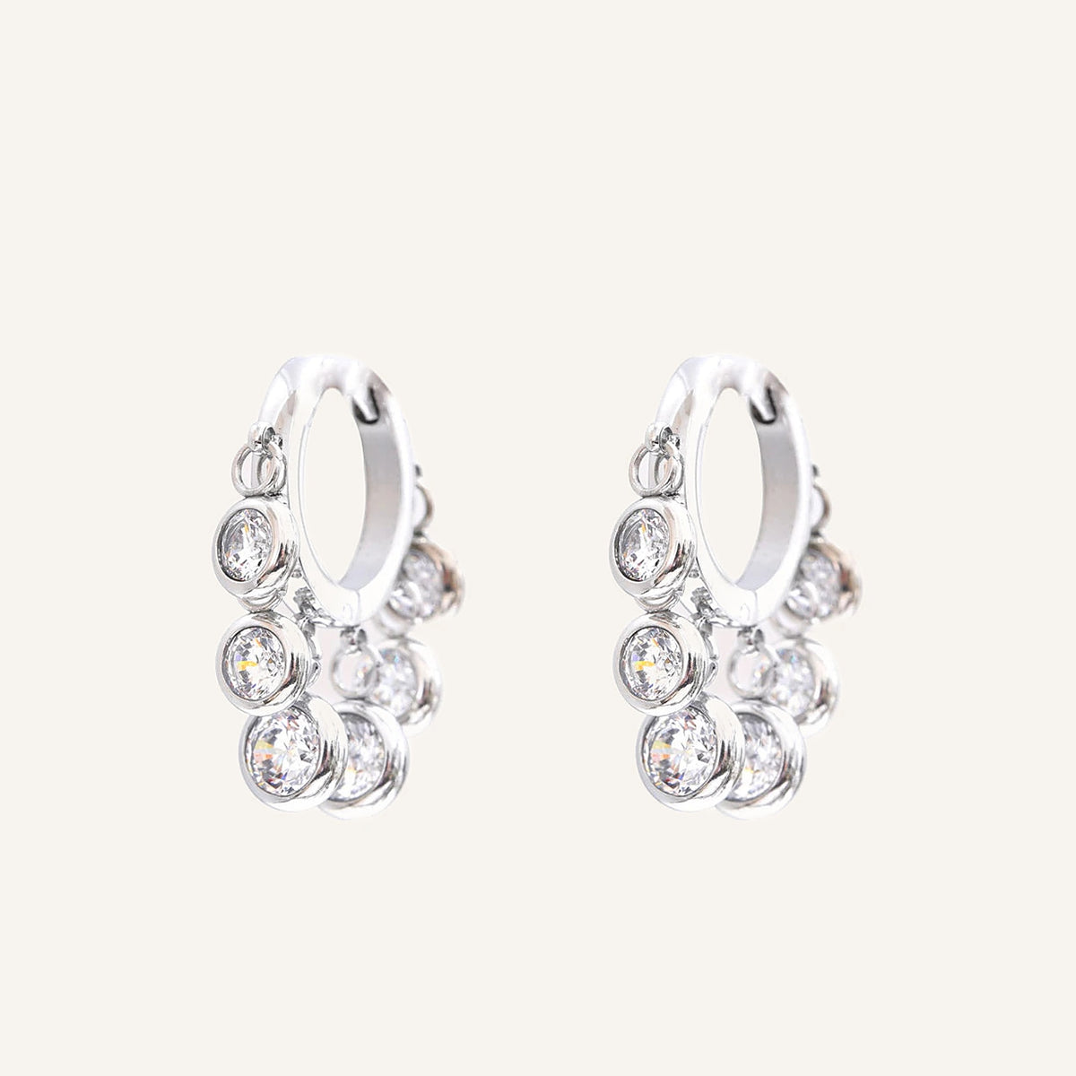 Créoles huggies avec pampilles en zircon coloré, zircons incolores, argentées, sur fond clair – Charmhabit