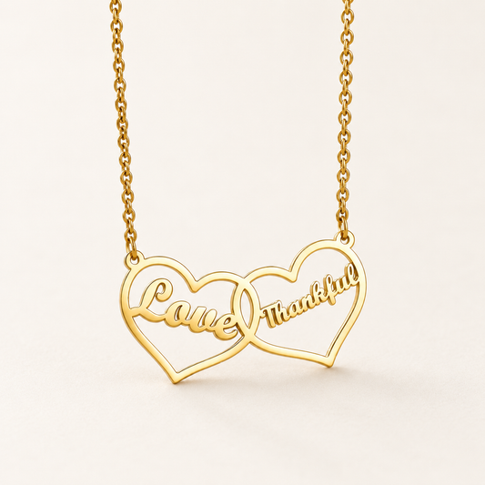 Goudkleurige ketting met twee verbonden hartjes en de voorbeeldgravures Love en Thankful op een rustige ivoorkleurige achtergrond