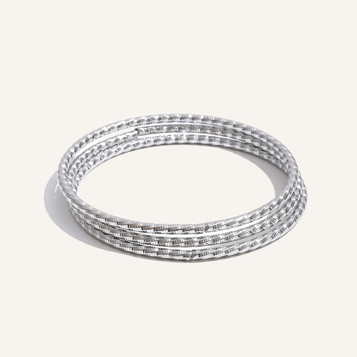 Set aus drei gedrehten Armbändern, silberfarben, auf hellem Hintergrund – Charmhabit