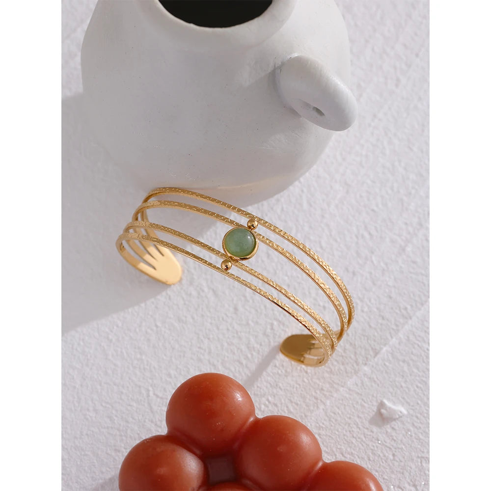 Offener Armreif mit grünem Stein, goldfarben, auf einer Vase – Charmhabit