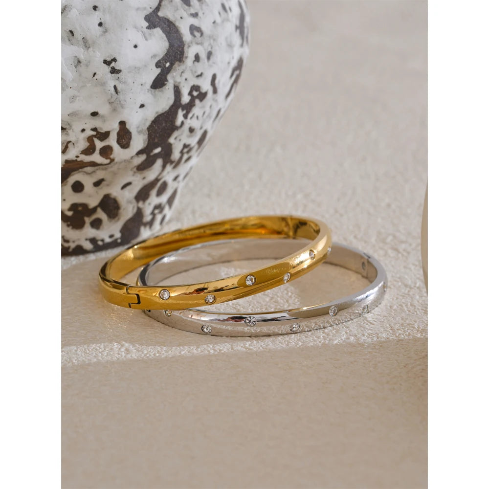 Bangle bracelet with zirconia, gold and silver tone, on a light surface – Charmhabit