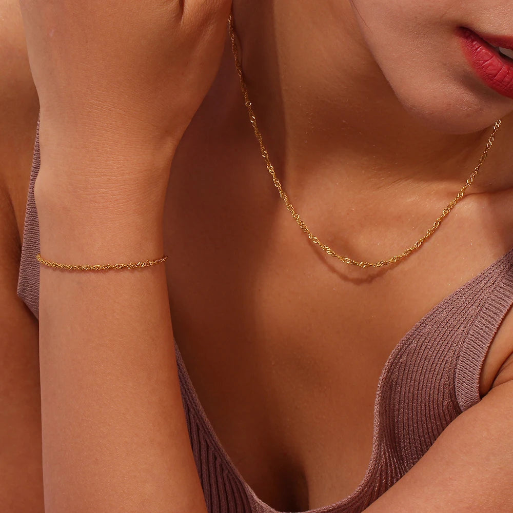 Parure composée d’un fin collier waterwave et d’un bracelet, dorée, portée, gros plan – Charmhabit