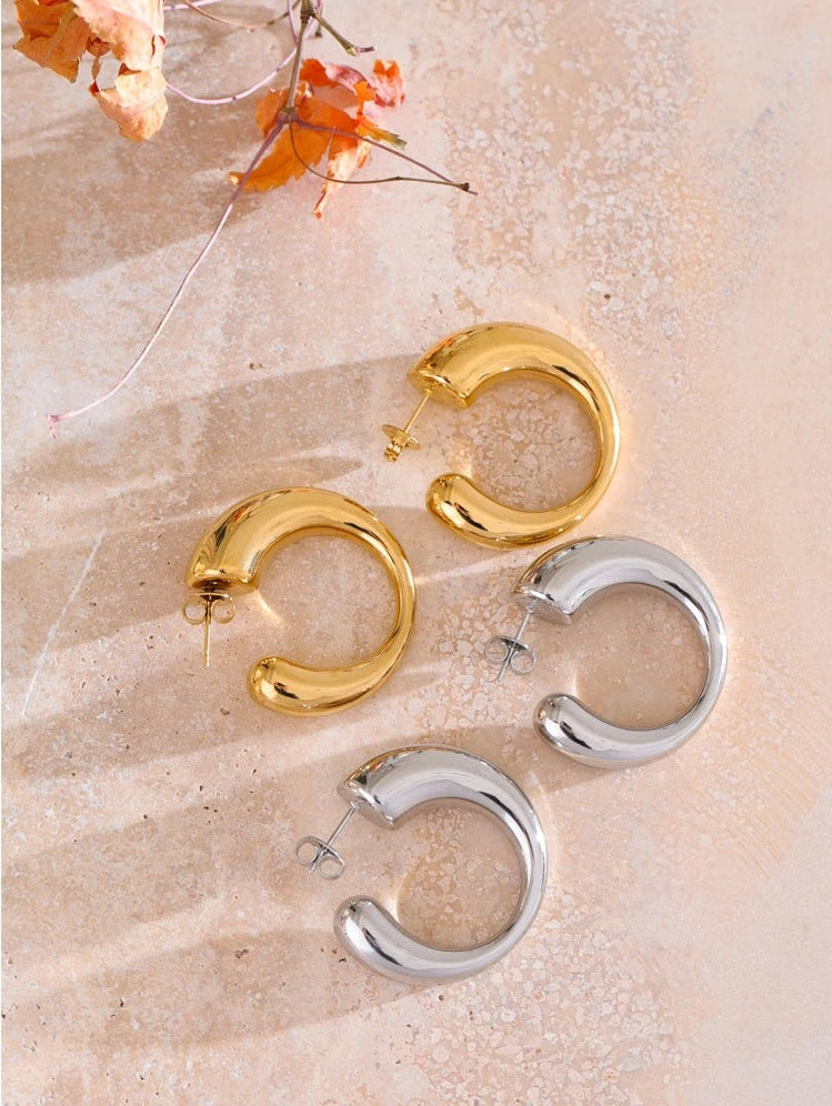 Chunky C-shaped hoop earrings in gold tone and silver tone on a light surface – Charmhabit