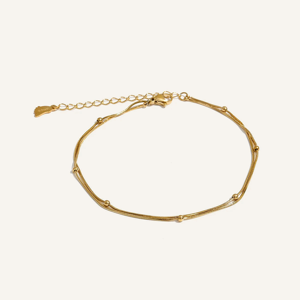 Doppeltes Fußkettchen mit Kügelchen, goldfarben, auf hellem Hintergrund – Charmhabit