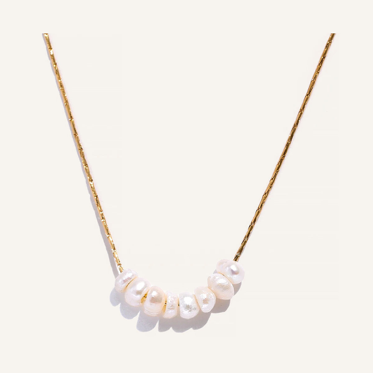 Feine Kette mit Perlen, goldfarben, auf hellem Hintergrund – Charmhabit