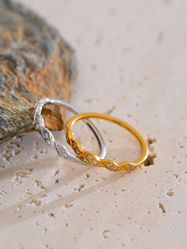 Gedrehter Ring mit Zirkonia, gold- und silberfarben, auf rauem Stein – Charmhabit