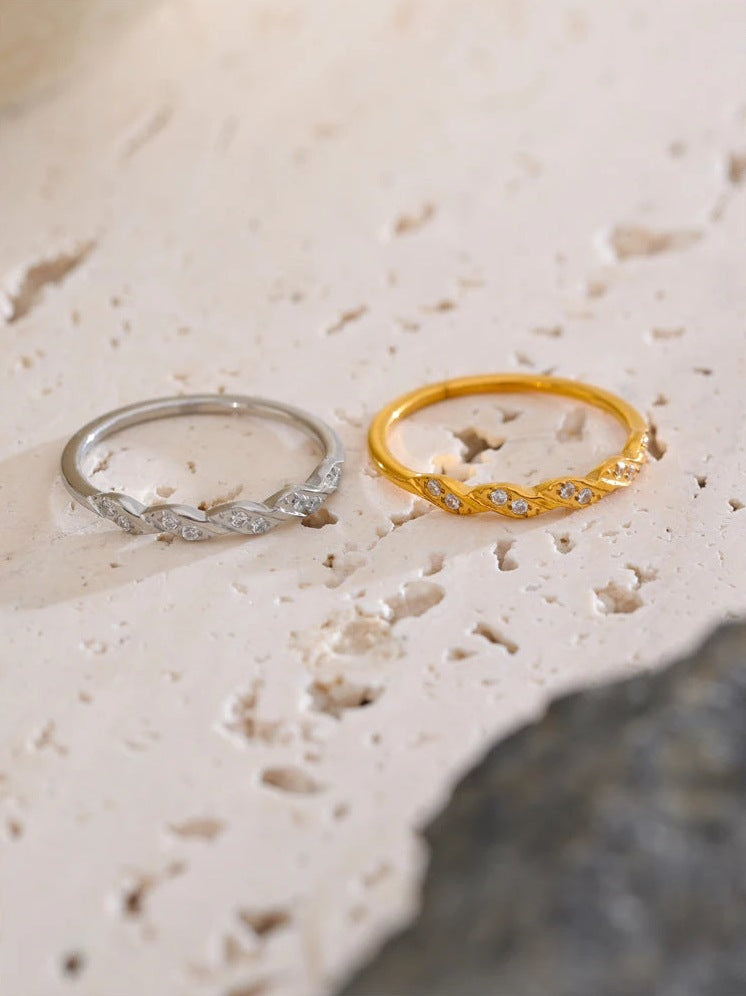 Gedrehte Ringe mit Zirkonia, gold- und silberfarben, auf hellem Stein – Charmhabit