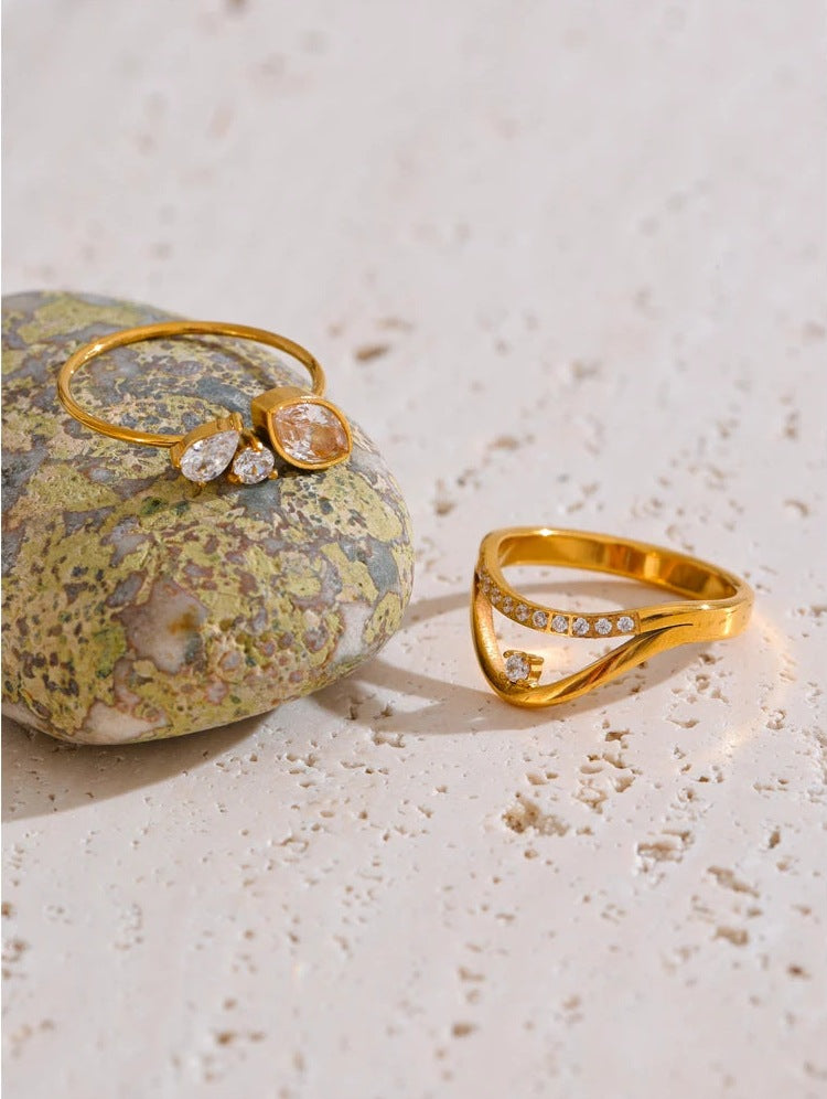 Goldfarbene Ringe mit Zirkonia auf einem farbigen Stein – Charmhabit