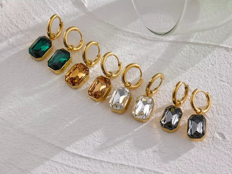 Huggie hoops with an octagonal crystal pendant in all colours, on a light surface – Charmhabit