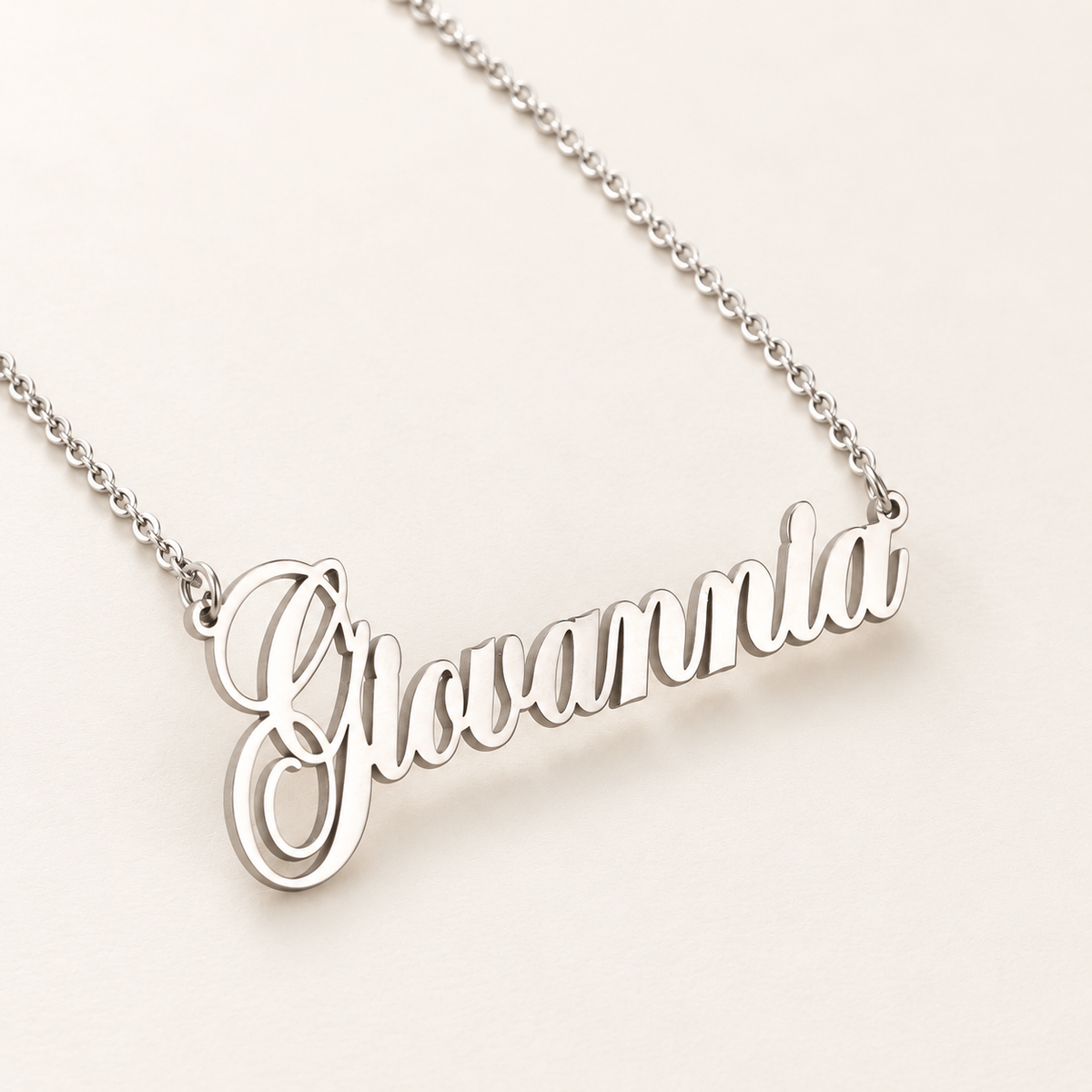 Zilverkleurige naamketting met de voorbeeldnaam Giovannia op een rustige ivoorkleurige achtergrond