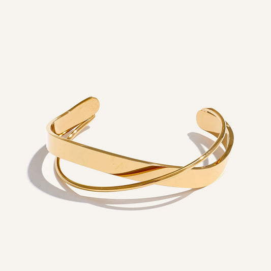 Open bracelet with crossed bands, gold tone, on a light background – Charmhabit